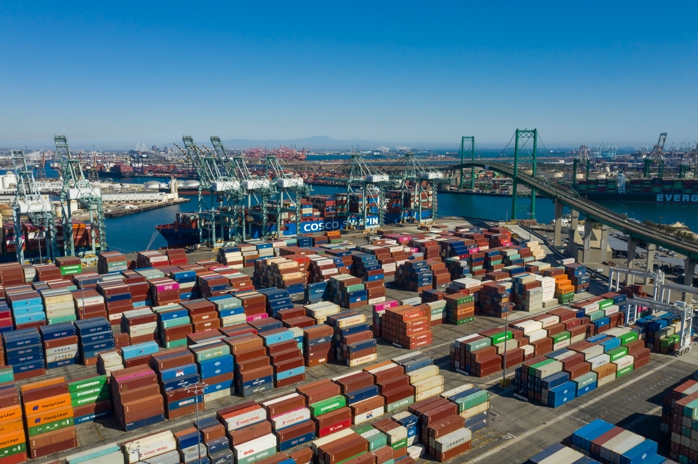 An aerial view of an international shipping port with stacked cargo containers, illustrating the impact of International Trade Tariffs on global supply chains and import costs.