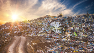 A large landfill filled with plastic waste and other discarded materials, with a bulldozer working in the background under a setting sun.
